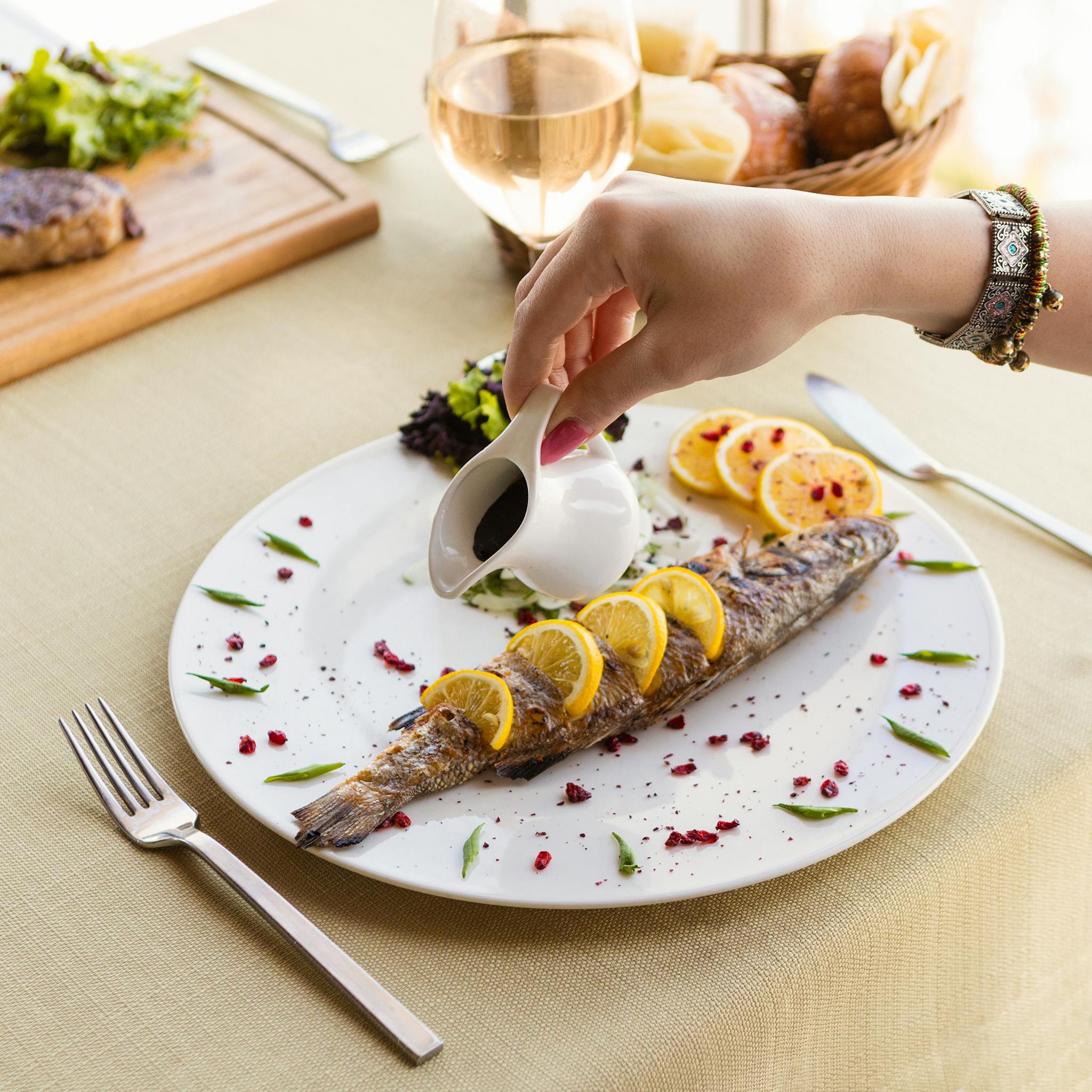 A gourmet grilled fish dish garnished with lemons being served at a stylish dining table.