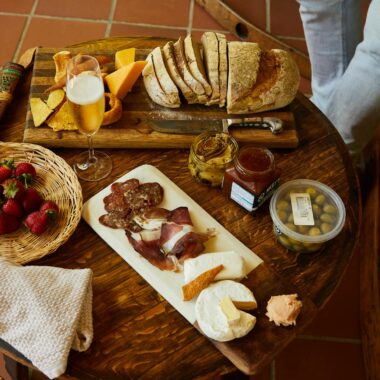 A rustic charcuterie board with bread, cheese, strawberries, and a drink on a wooden table.
