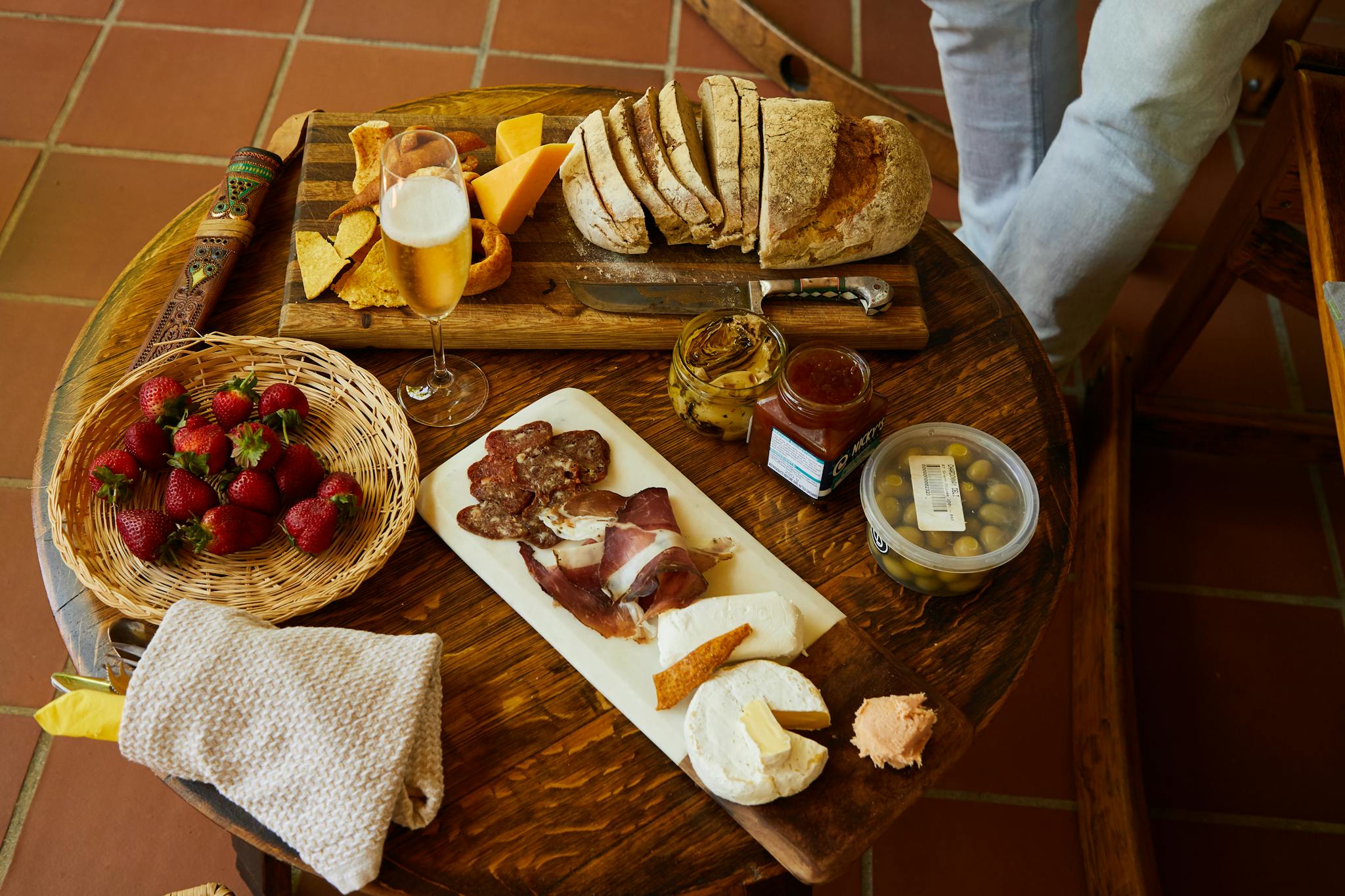 A rustic charcuterie board with bread, cheese, strawberries, and a drink on a wooden table.