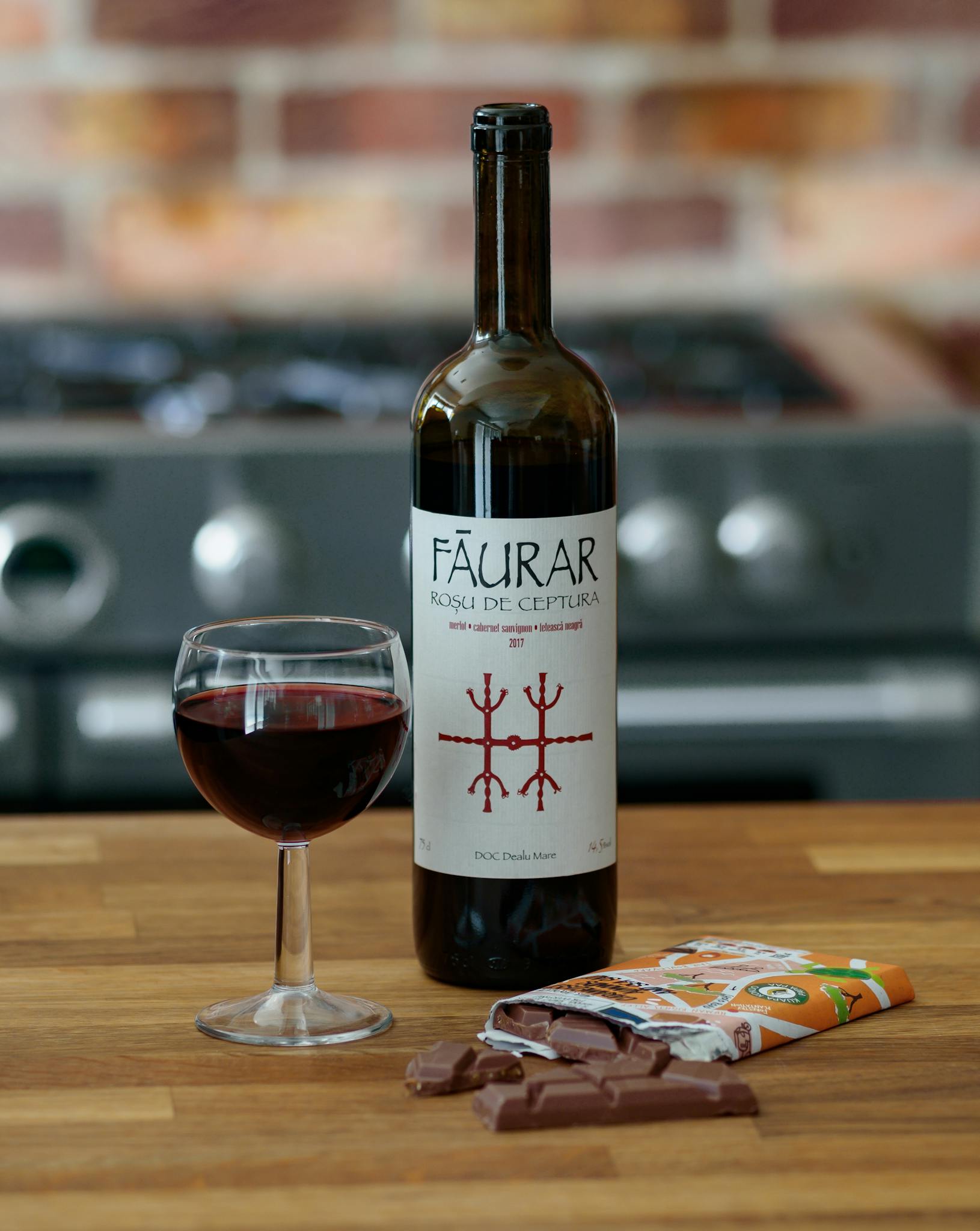 Red wine bottle and glass with chocolate on a wooden counter indoors.